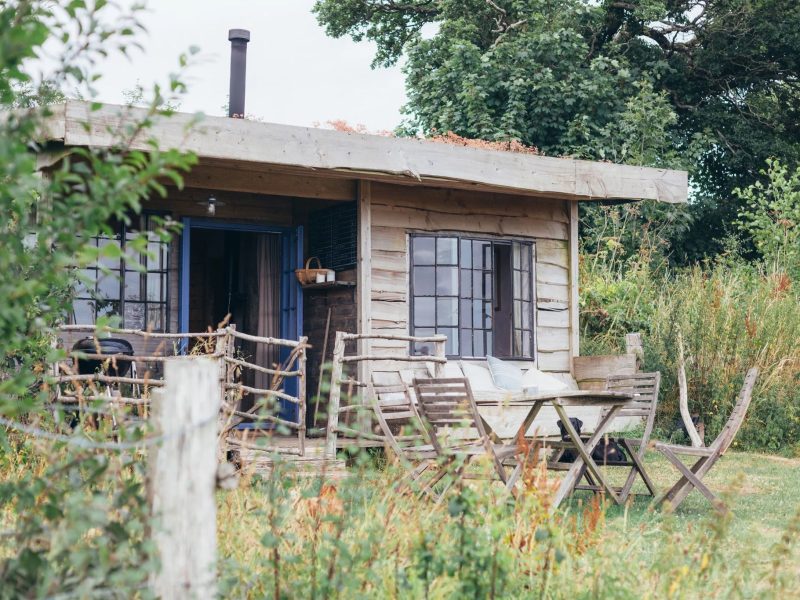 The Gardener's Shed at Mello View, a timber cabin with a sun terrace and outdoor table set in a wildflower meadow in Somerset