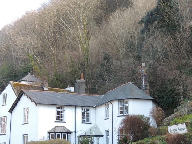 The white-painted, Grade II-listed Orchard House Hotel beneath the steep wooded slopes of the Watersmeet Valley in Lynmouth, Devon