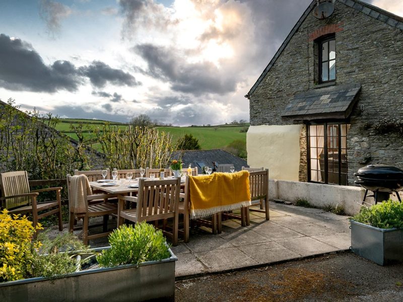 BBQ terrace at Martingale cottage, Pitt Farm, with outdoor dining table, flower beds and views over the South Hams countryside