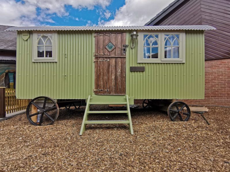 Sage-green shepherd’s hut on cast-iron wheels with wooden steps in the courtyard of the Stonehenge Inn