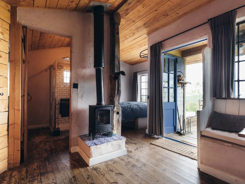 Open-plan interior of the Gardener's Shed with a wood burner, wide wooden floorboards and a window seat