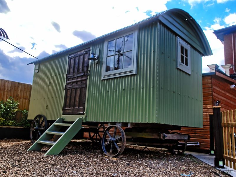 Green shepherd’s hut with arched windows and a stable-style door in the gravel courtyard at the Stonehenge Inn