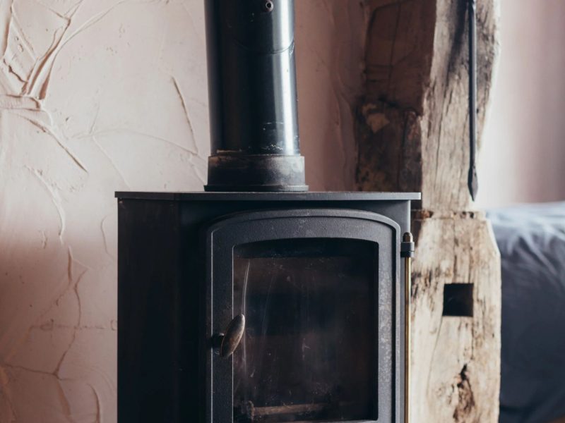 Cast-iron wood burner beside a weathered oak beam and textured lime-plaster wall in the off-grid cabin at Mello View, ideal for drying off after a muddy dog walk