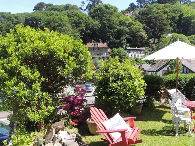 Sunny garden terrace at Orchard House Hotel with deckchairs, a red Adirondack chair and a parasol, looking over the treetops of Lynmouth