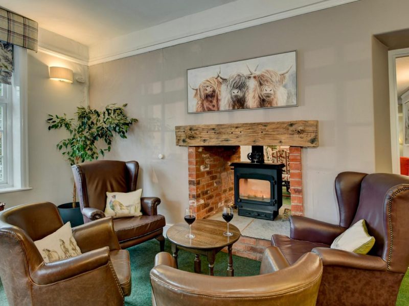 Lounge at The Crown Hotel with leather armchairs gathered round a wood burner in a stone fireplace