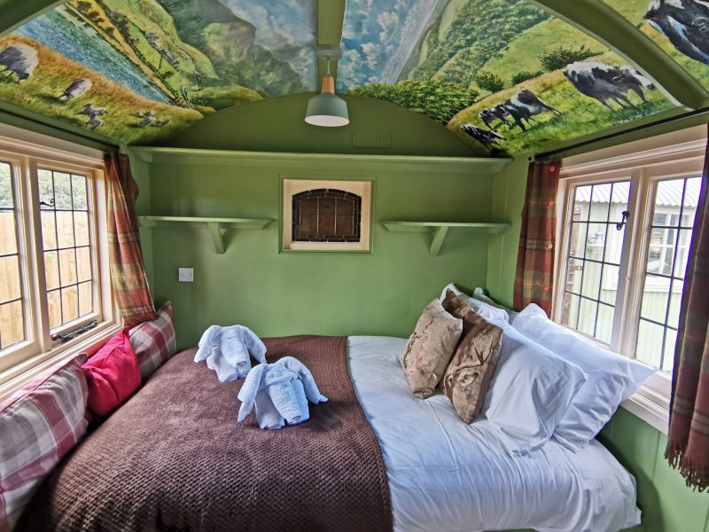 Double bed with tartan and patterned cushions under a hand-painted countryside ceiling in one of the courtyard rooms at the Stonehenge Inn