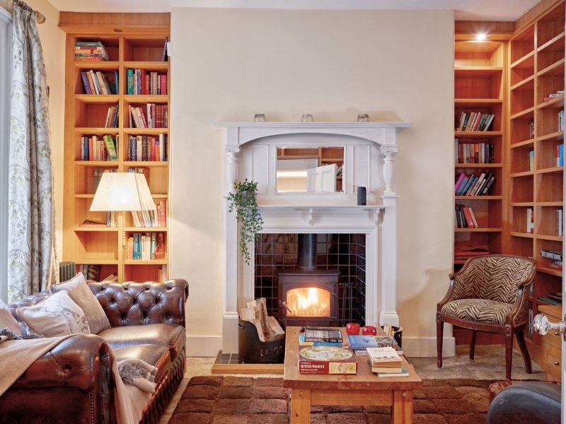 Snug at Upwey House with a leather Chesterfield sofa, a lit log burner and floor-to-ceiling bookshelves either side