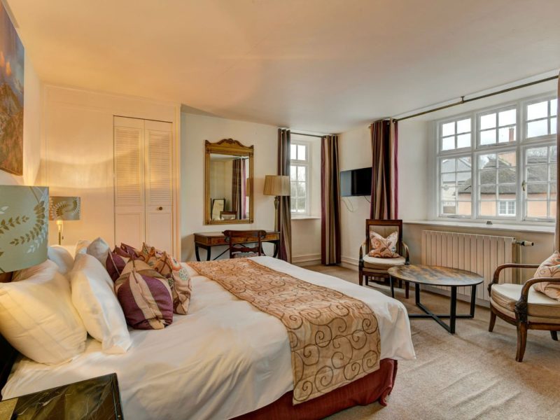 King-size bedroom at The Crown Hotel with patterned cushions, a sitting area with armchairs and tall windows