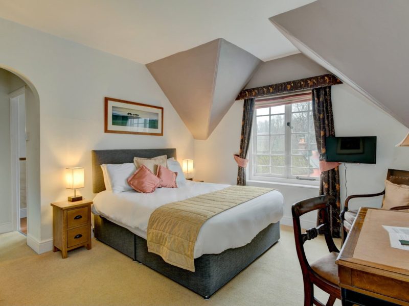 Double room at The Crown Hotel under a sloping ceiling, with a grey upholstered bed and a desk by the window